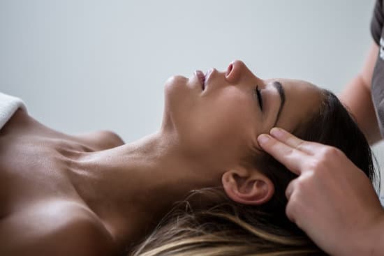 Side view of relaxed woman lying on table in SPA salon and having massage of face keeping eyes closed